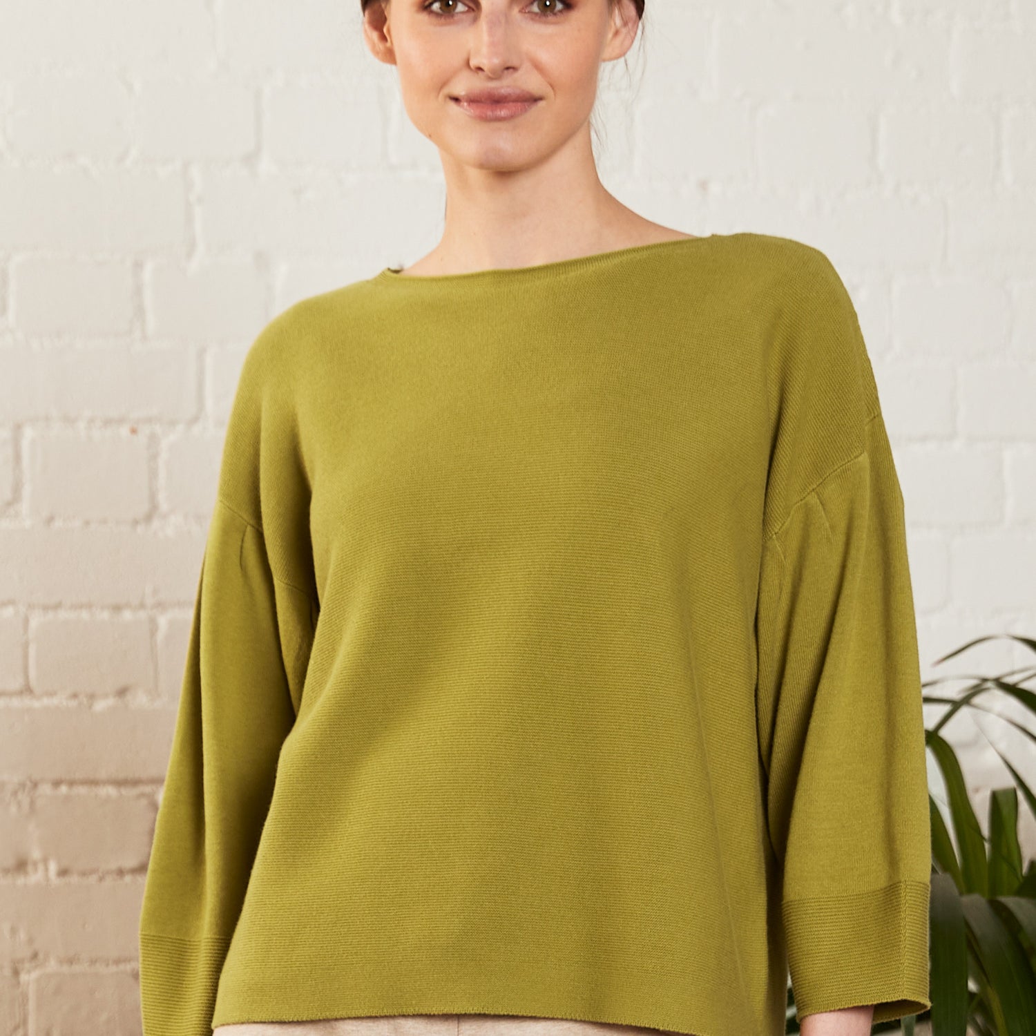 A woman wearing an alpine color jumper is in front of a white wall.