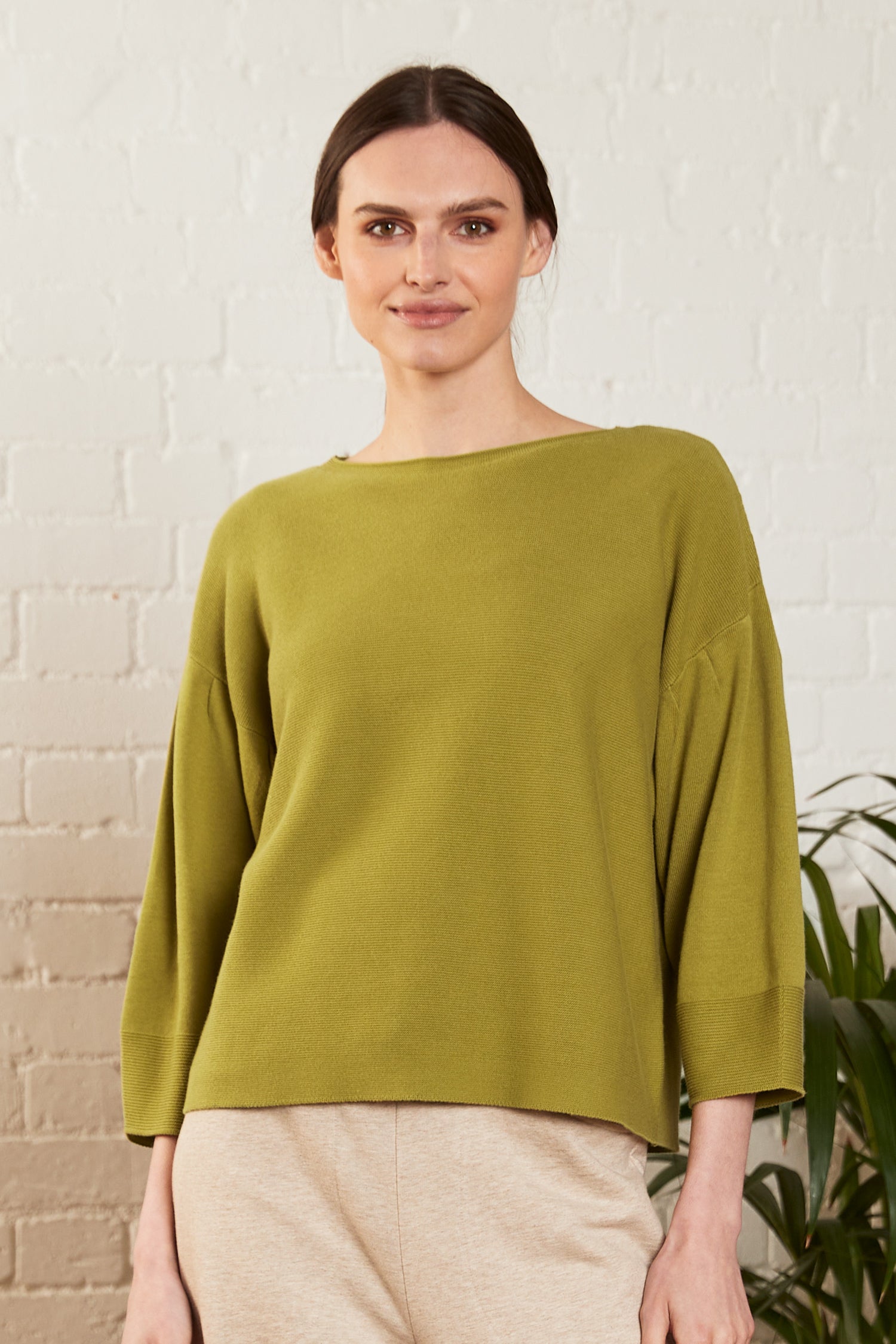 A woman wearing an alpine color jumper is in front of a white wall.