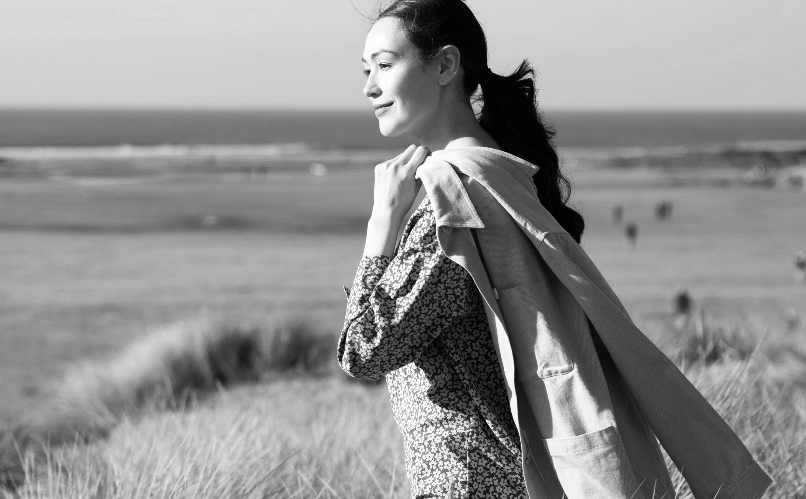 Woman standing in a field holding a jacket, black and white photo